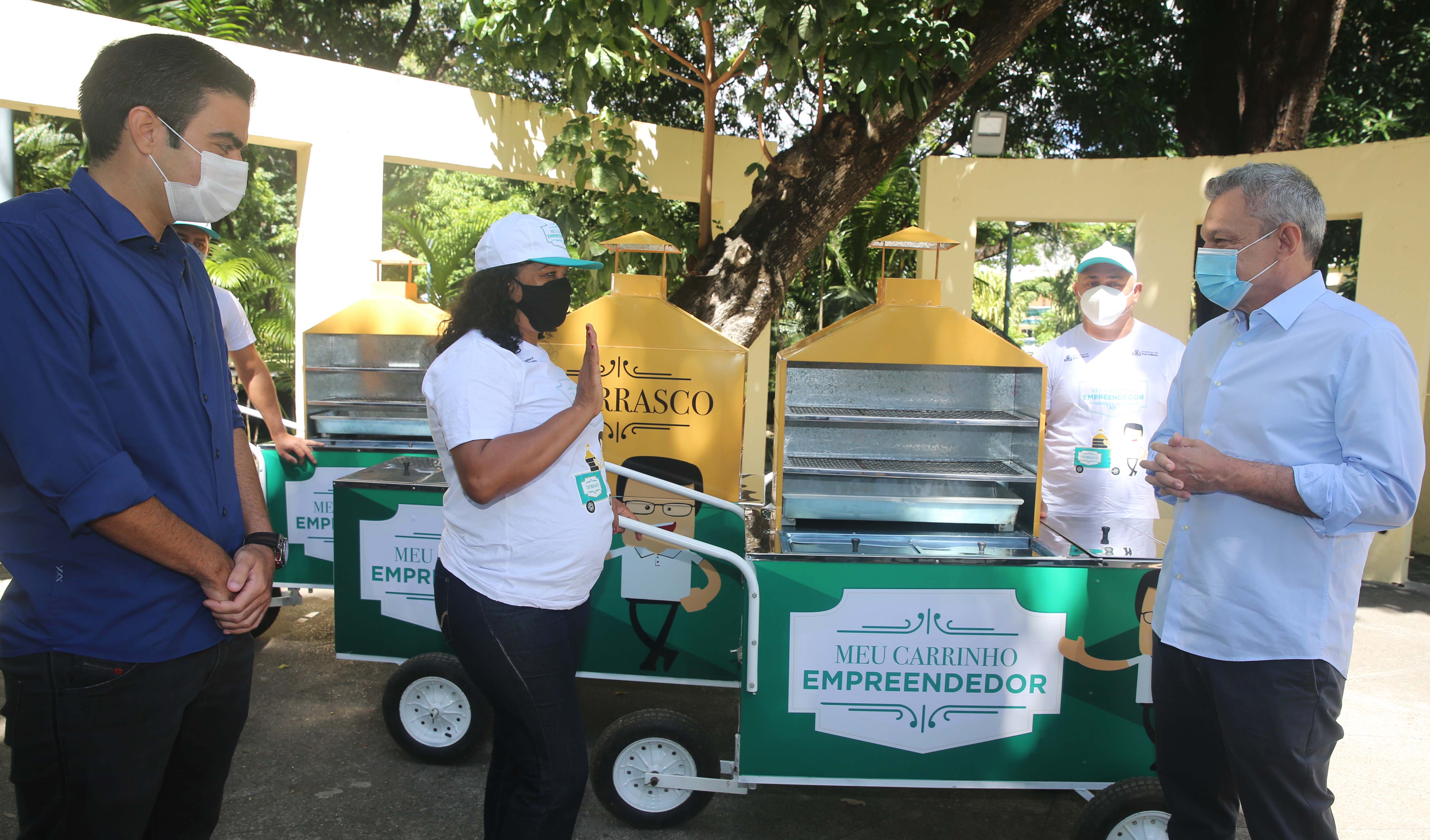 três pessoas em frente a um carrinho de churrasco, o carrinho pe verde e tem um espaço para uma churrasqueira pequena